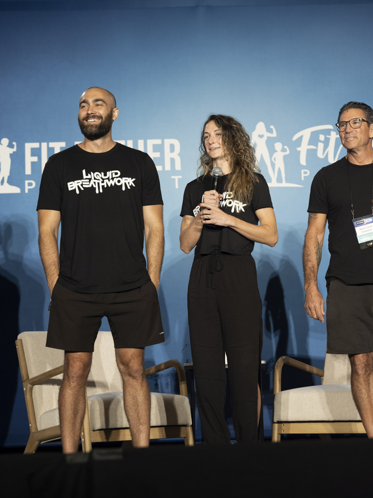 Ryan and Shelby on stage at Fit Father Project conference in Liquid Breathwork shirts