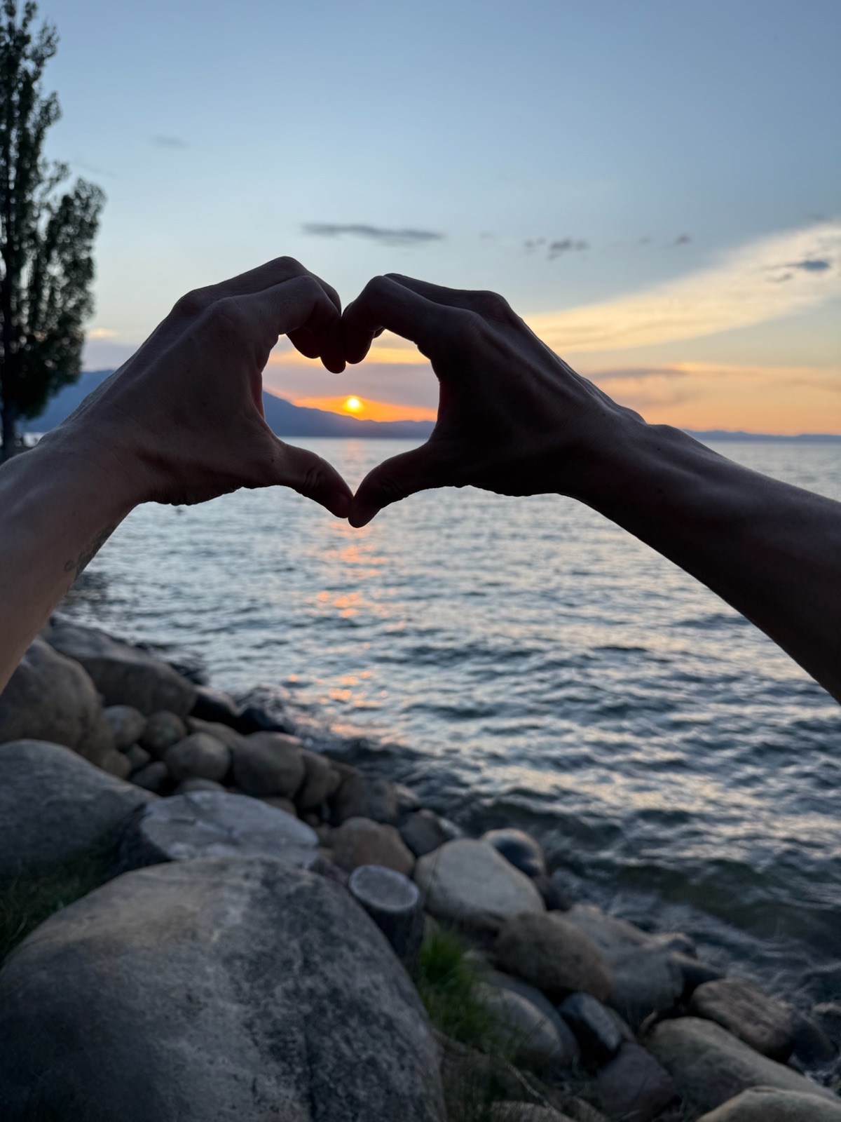 Hands forming a heart around the sunset over Lake Tahoe during a Liquid Breathwork intensive